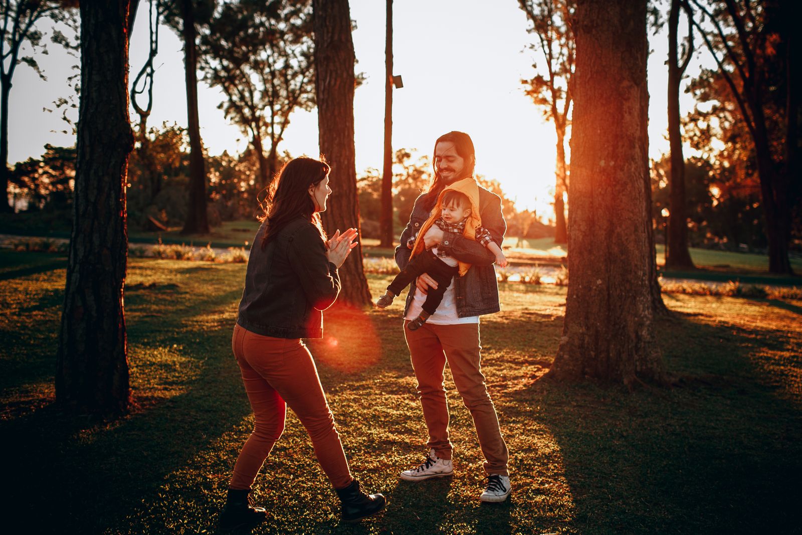 A mum and dad playing with their baby in a park at sunset